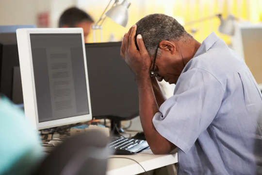 man holding head in his hand in front of a computer screen